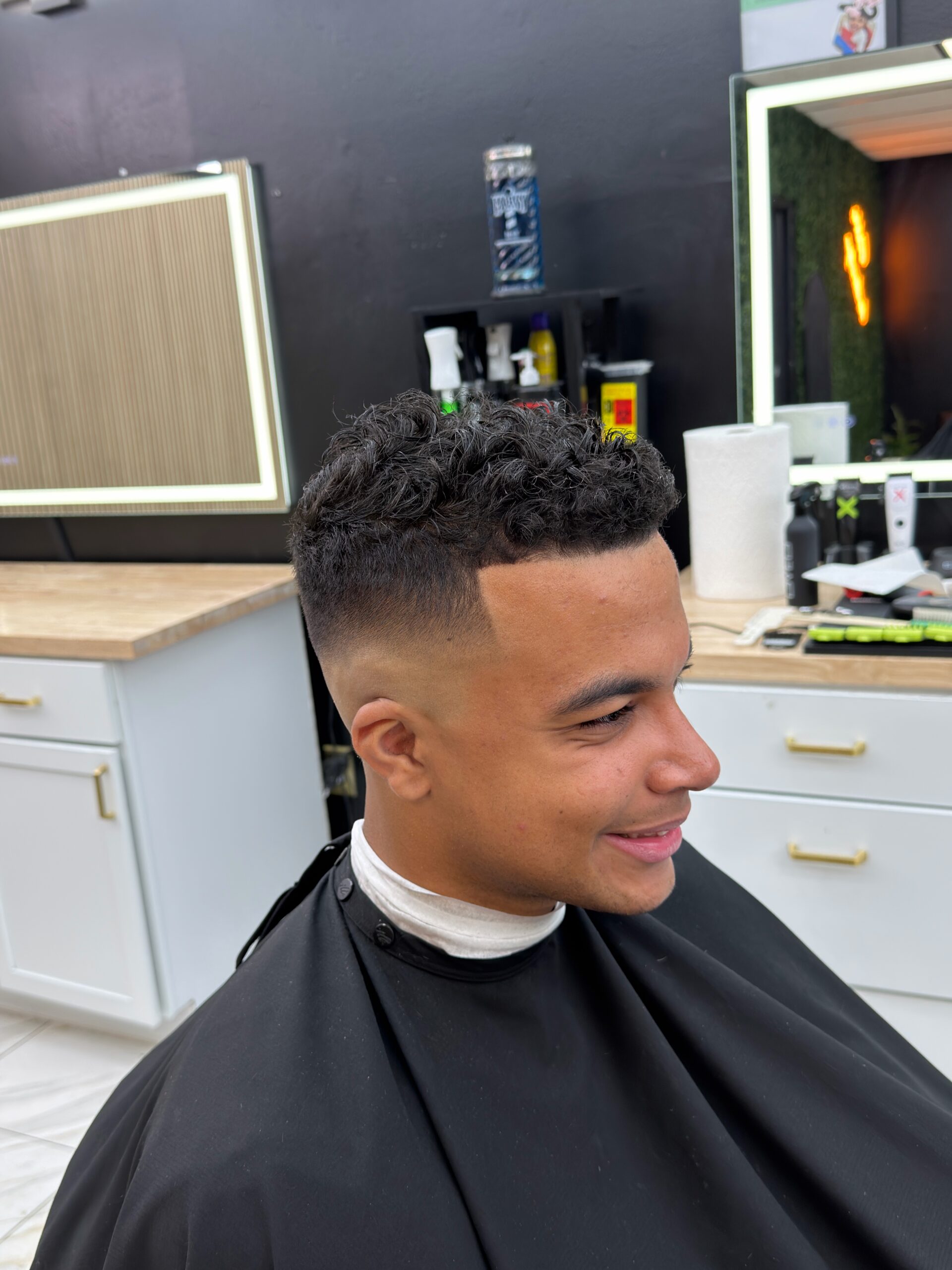 A young man with a fresh fade in a Golden Barbershop chair's curly hair under professional lighting at Golden Barbershop.